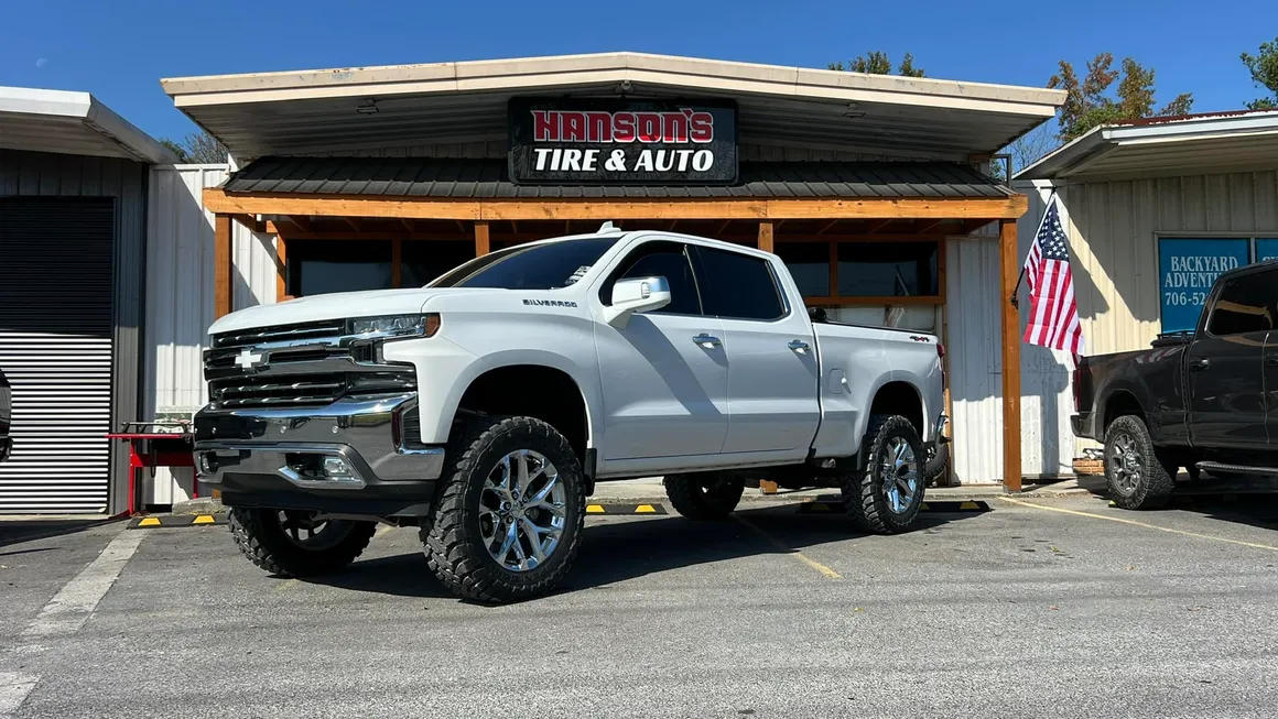 A white truck is parked in front of a tire and auto shop.