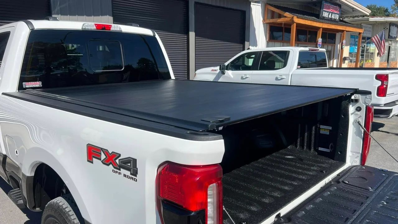 A white truck with a black tonneau cover is parked in front of a building.