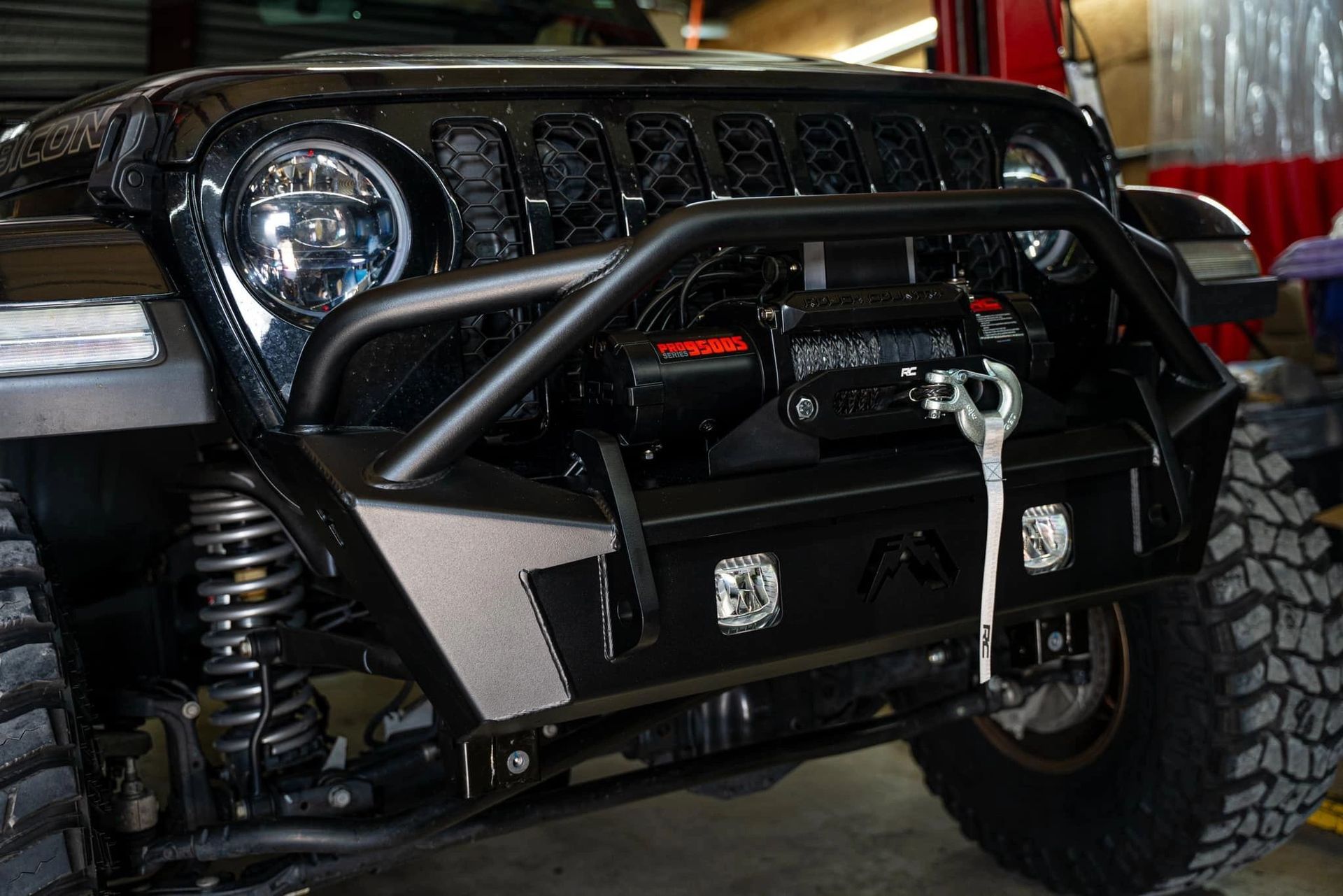 A black jeep with a winch attached to the front bumper is parked in a garage.