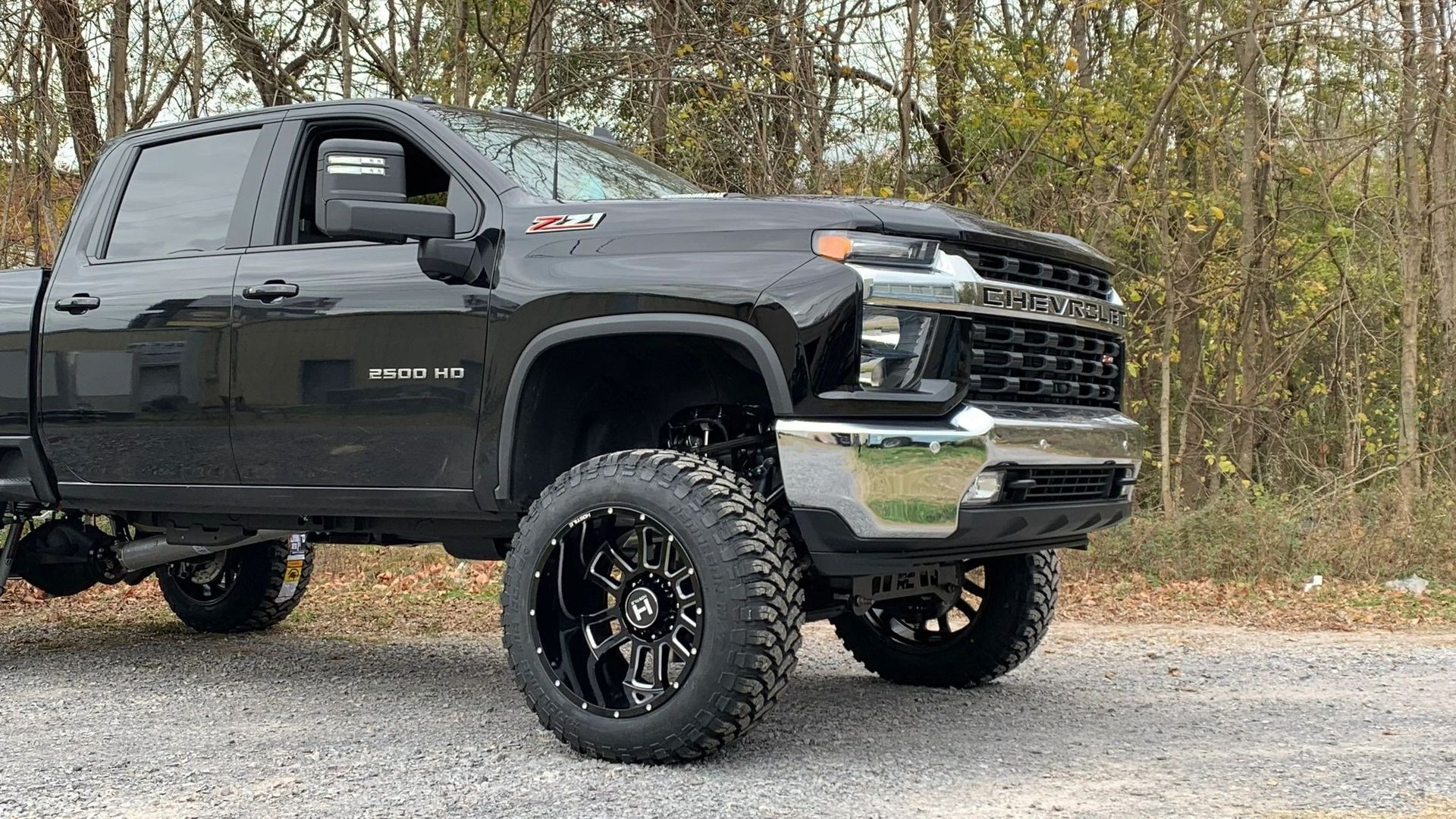 A black truck with black wheels and tires is parked on a gravel road.