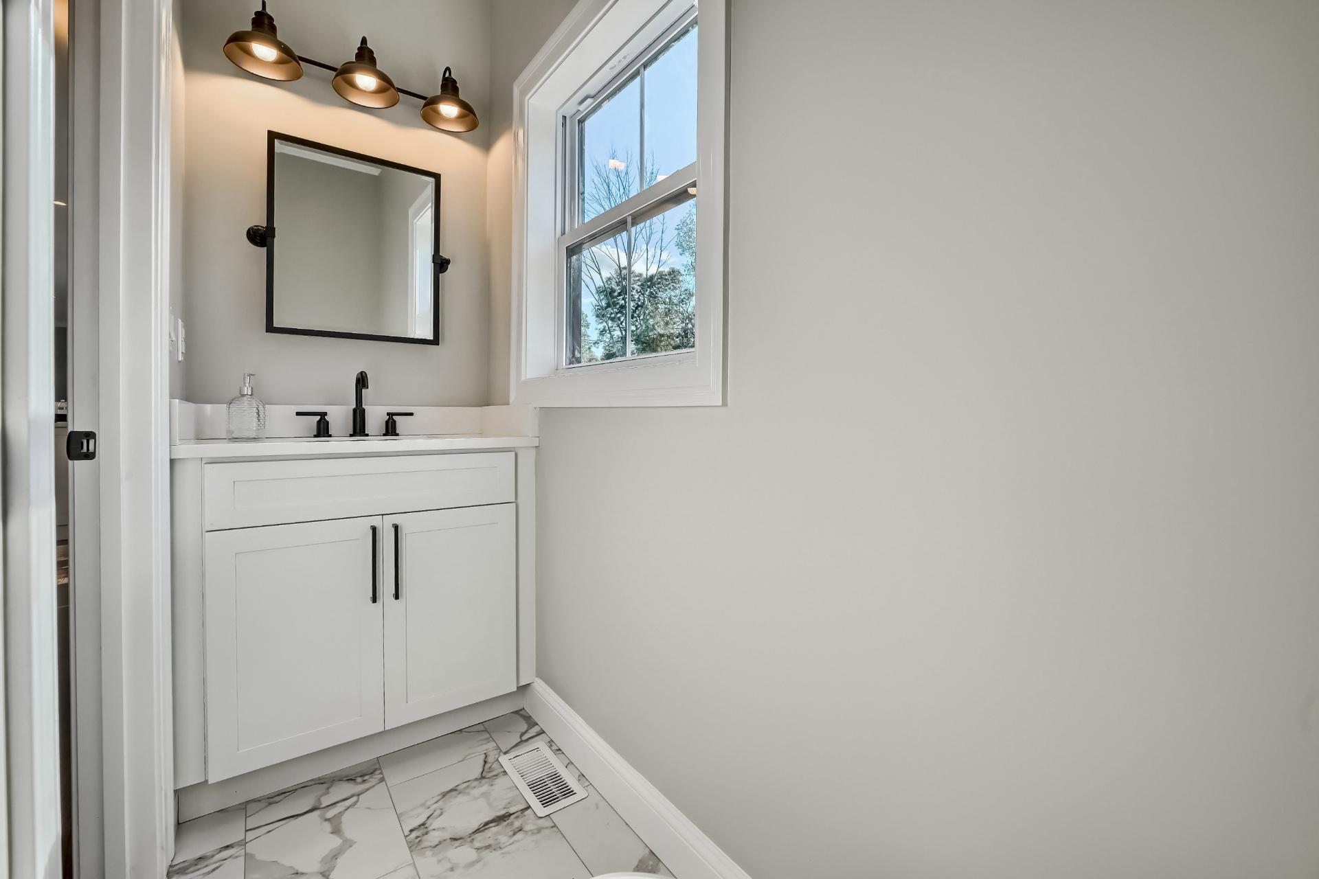A bathroom with a sink , mirror and window.