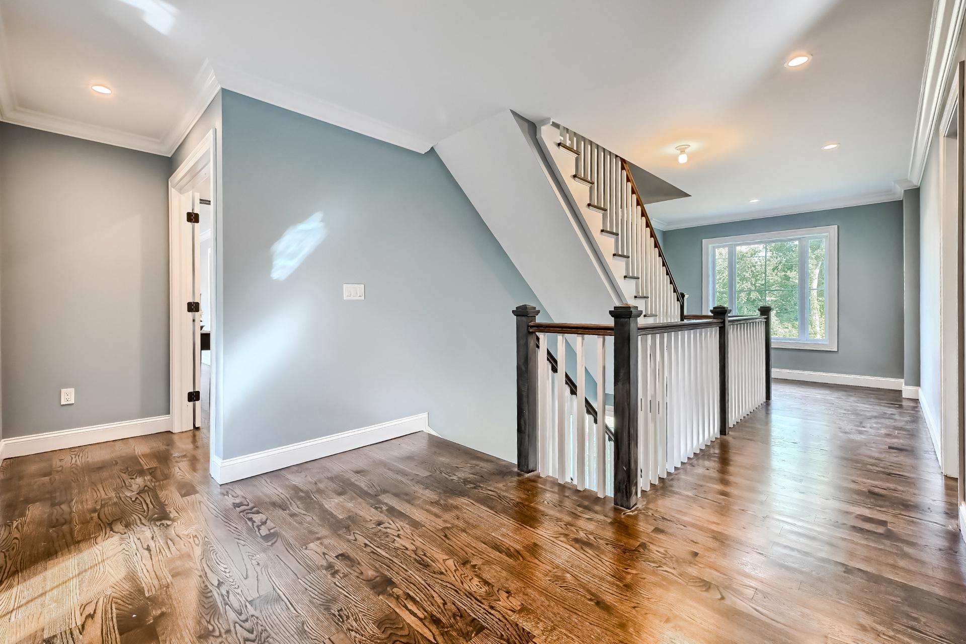 An empty hallway with hardwood floors and stairs in a house.