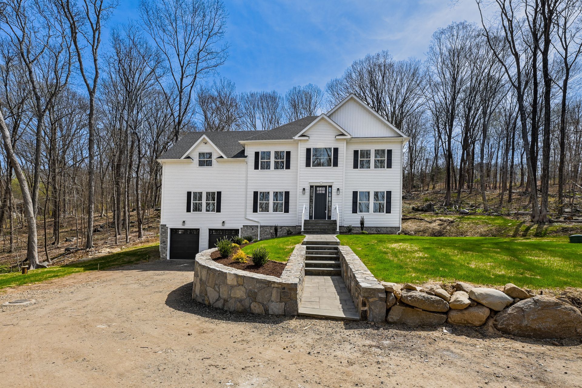 A large white house is surrounded by trees and a gravel driveway