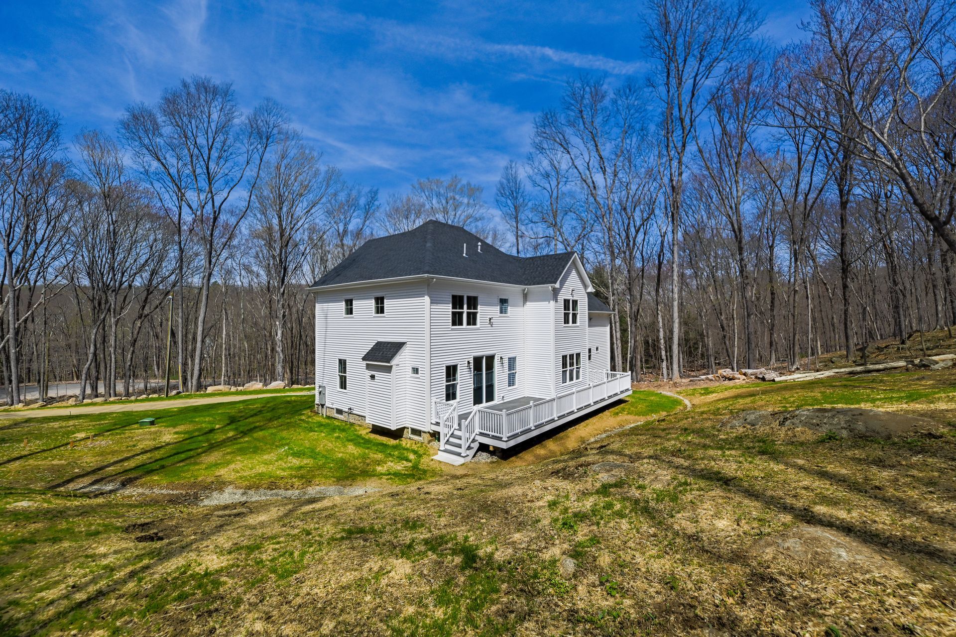 A white house with a large deck in the middle of a grassy field surrounded by trees.