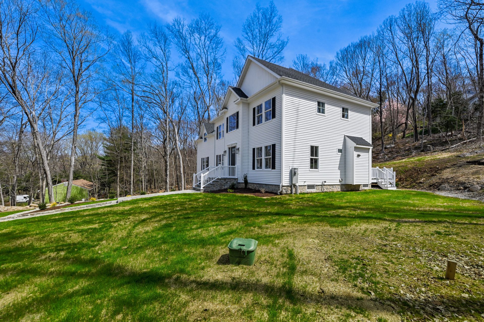 A large white house is sitting on top of a lush green hillside surrounded by trees.