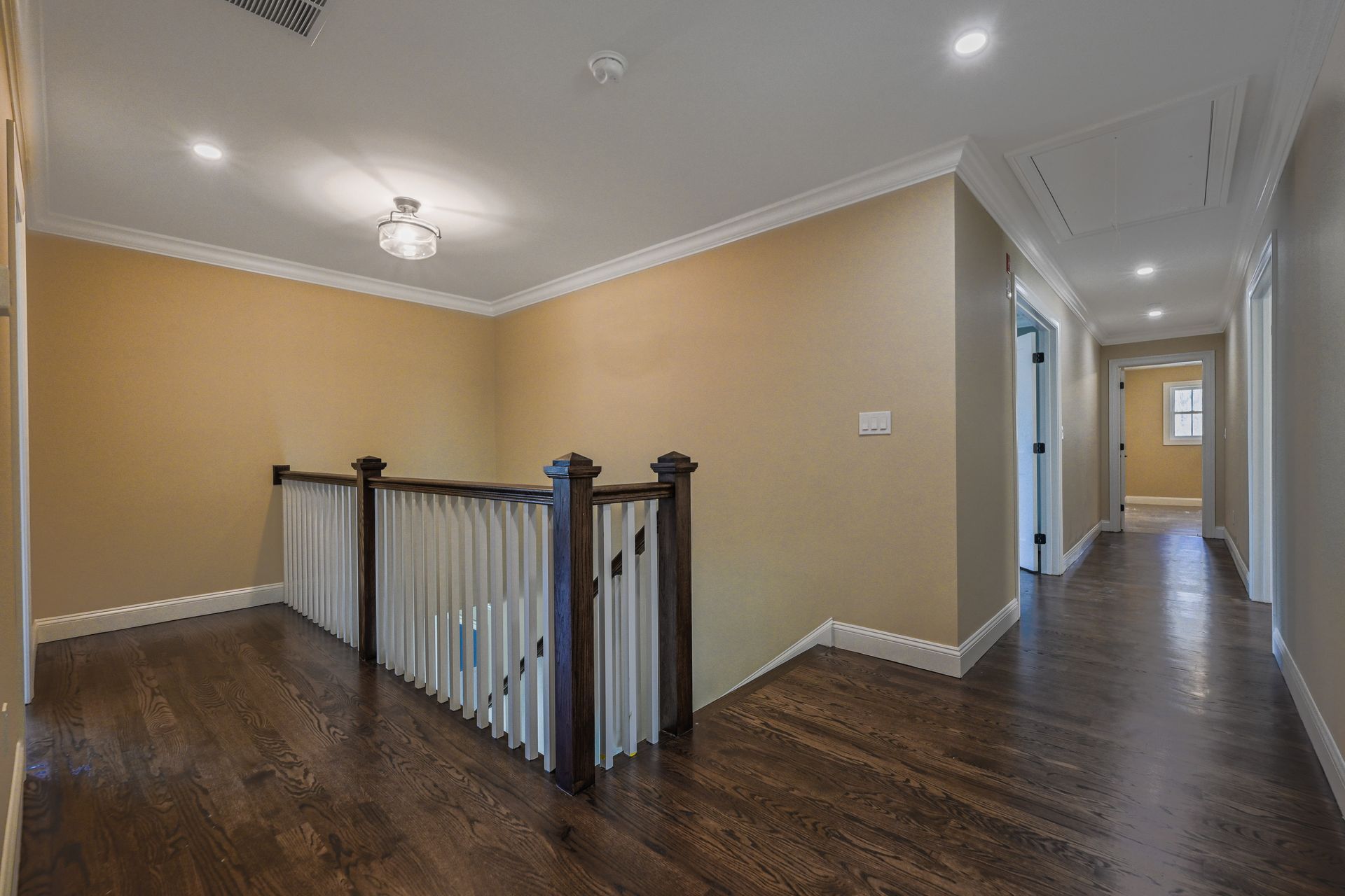 An empty hallway with hardwood floors and a staircase in a house.