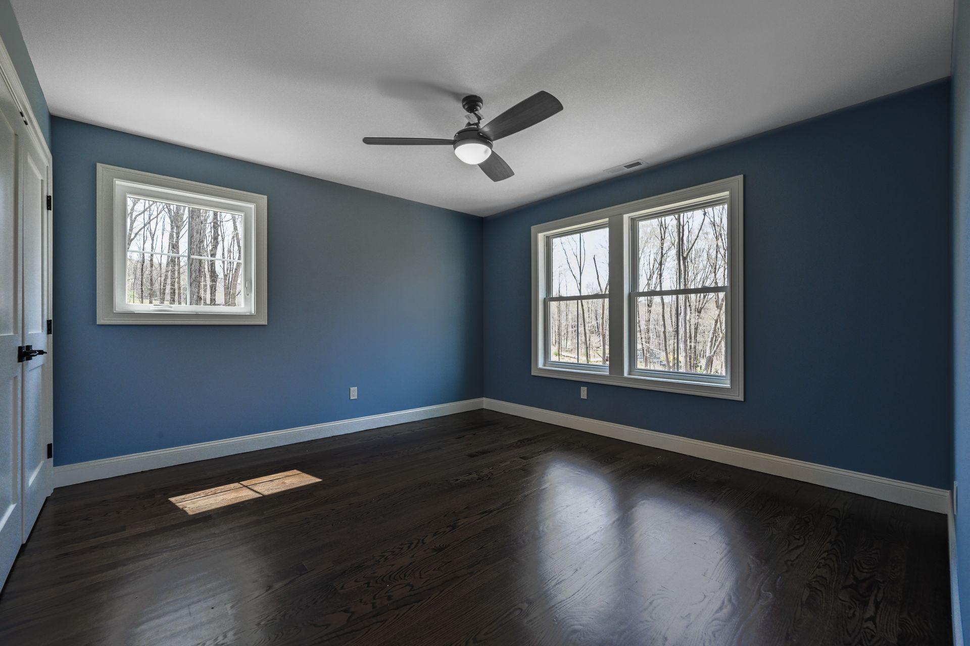 An empty bedroom with blue walls and a ceiling fan.