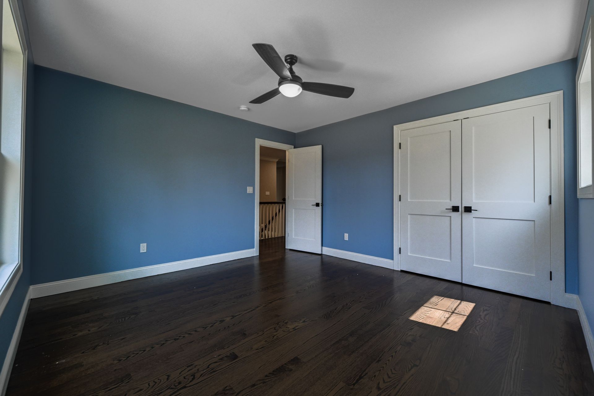 An empty bedroom with blue walls and a ceiling fan.