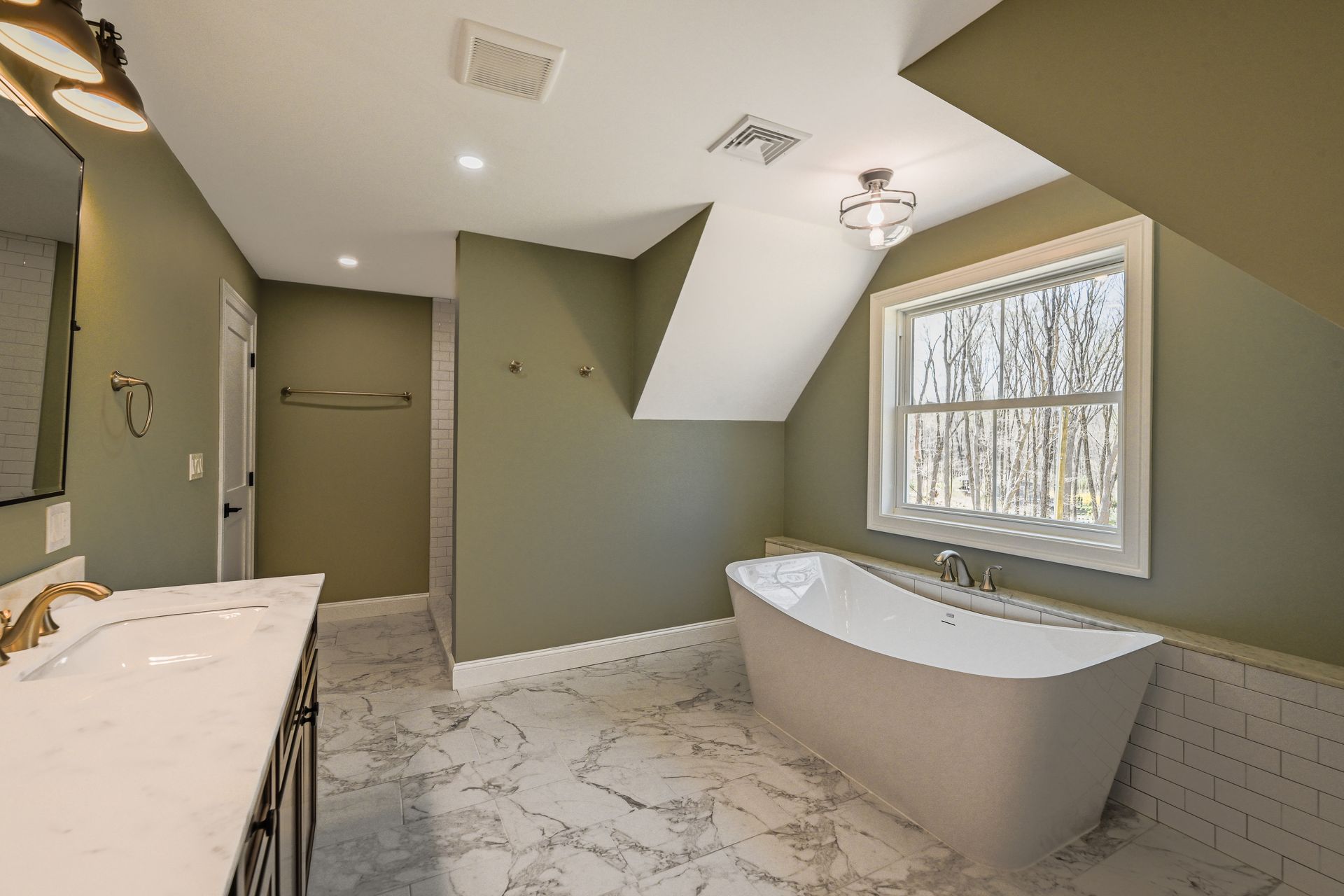 A bathroom with a tub , sink , mirror and window.