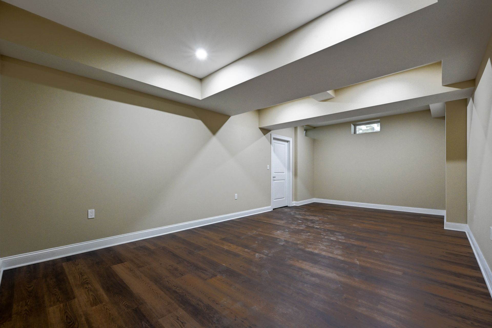 An empty basement with hardwood floors and beige walls.