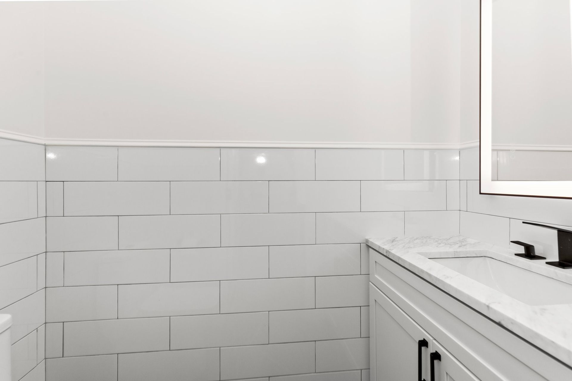 A bathroom with white tiles , a sink , and a mirror.