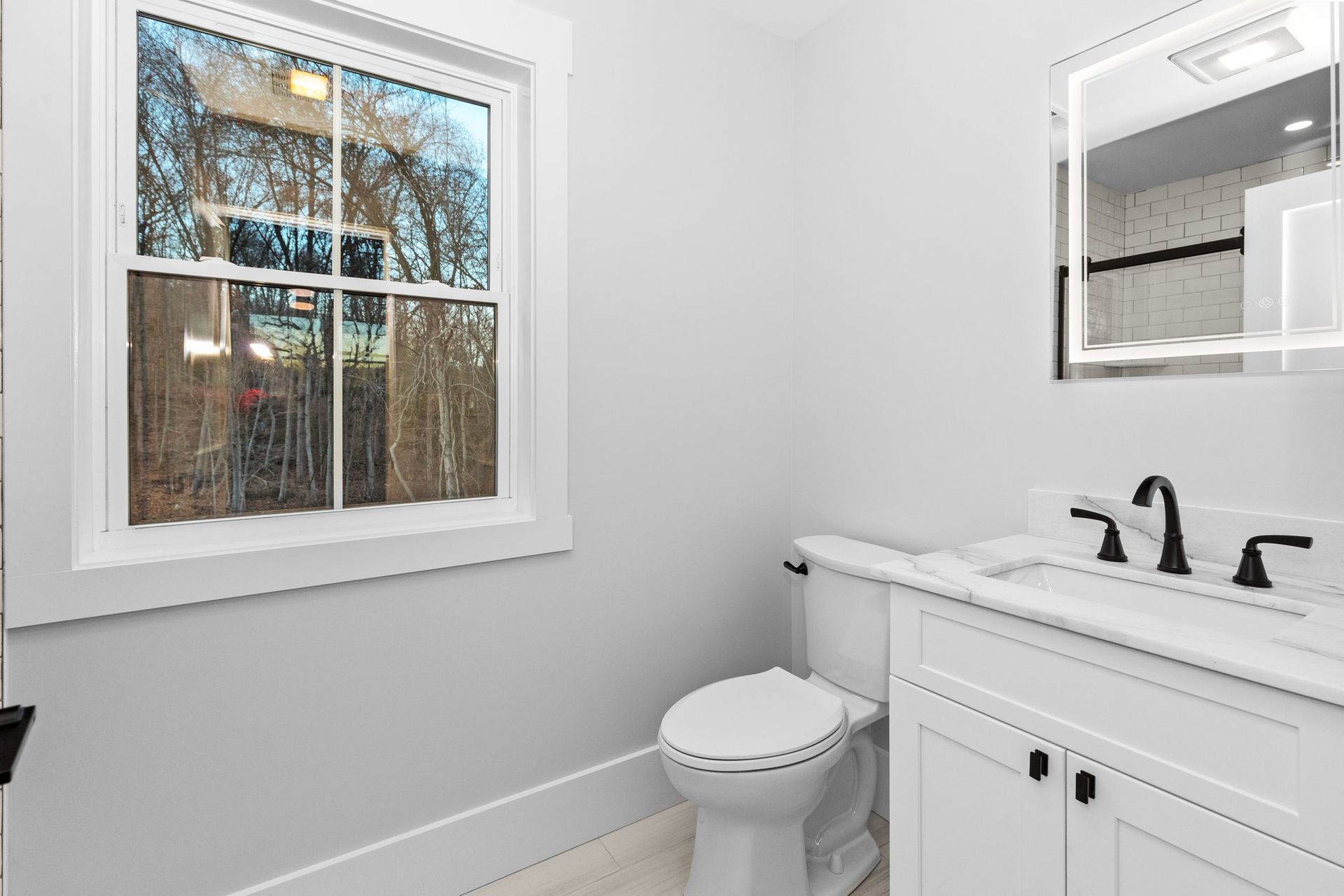 A bathroom with a toilet , sink , mirror and window