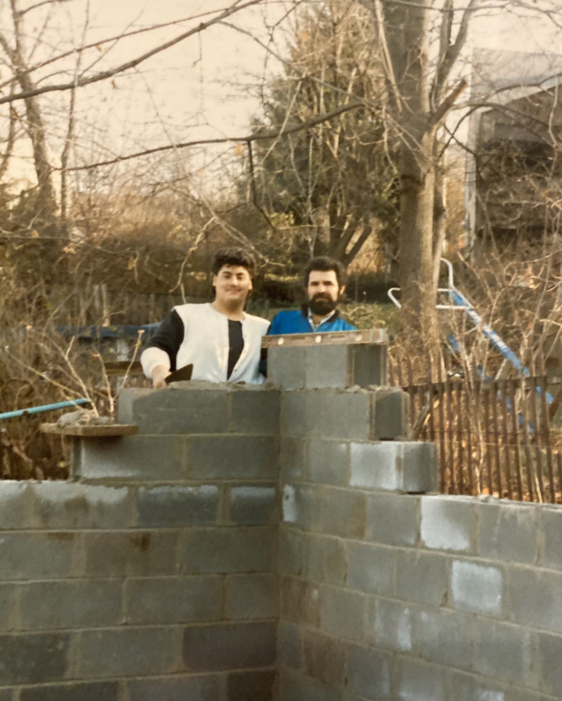 Two men standing on a brick wall with trees in the background