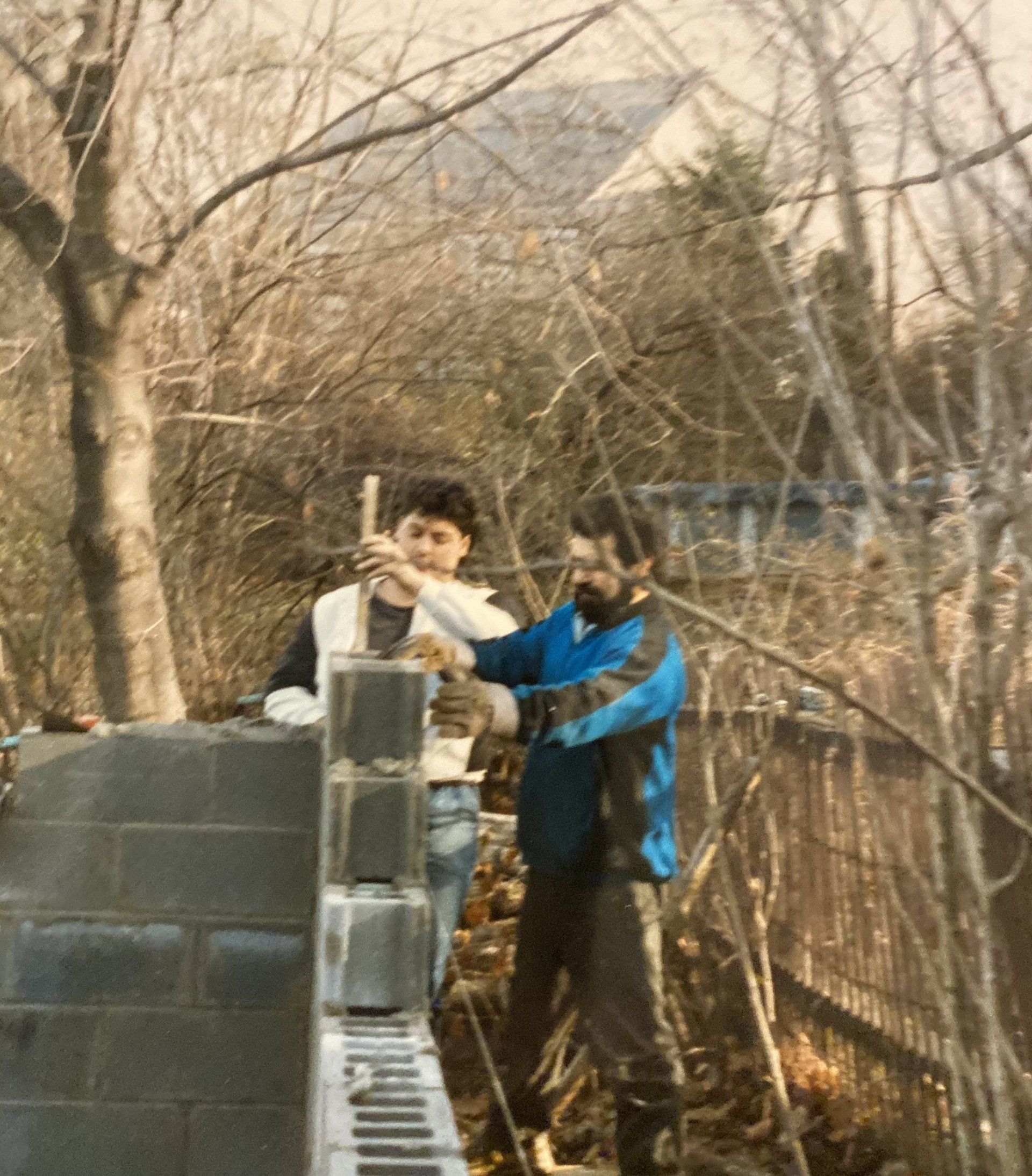 Two men are working on a brick wall in the woods
