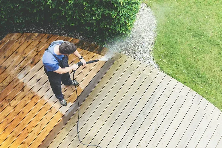 A man is cleaning a wooden deck with a high pressure washer.