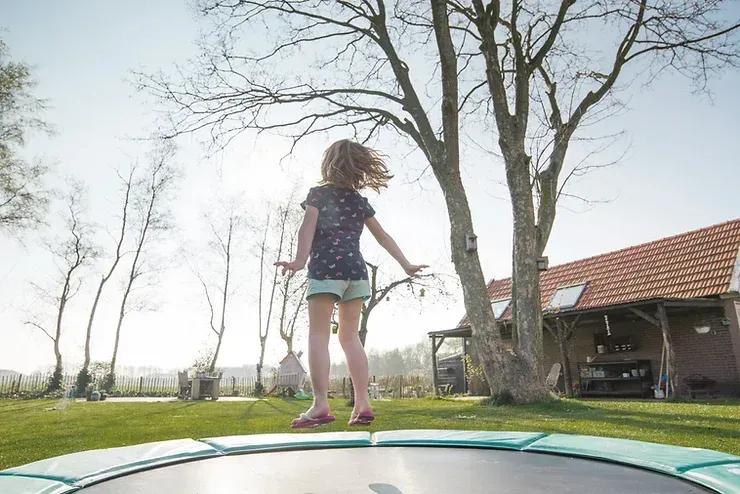 A little girl is jumping on a trampoline in a yard.