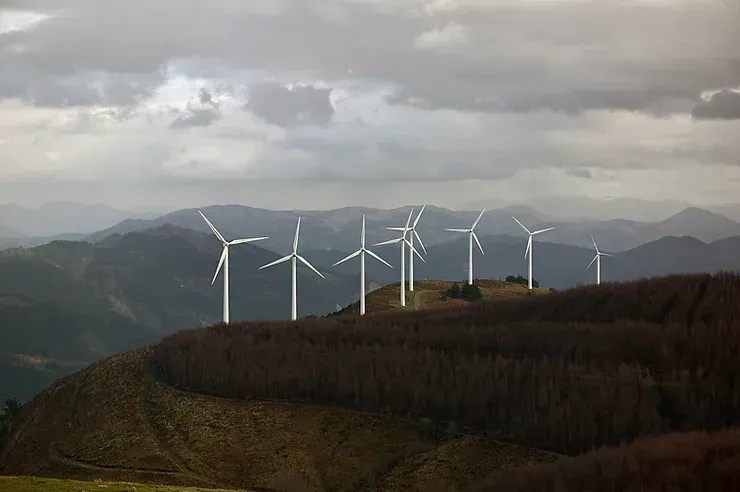 A row of wind turbines on top of a hill with mountains in the background.