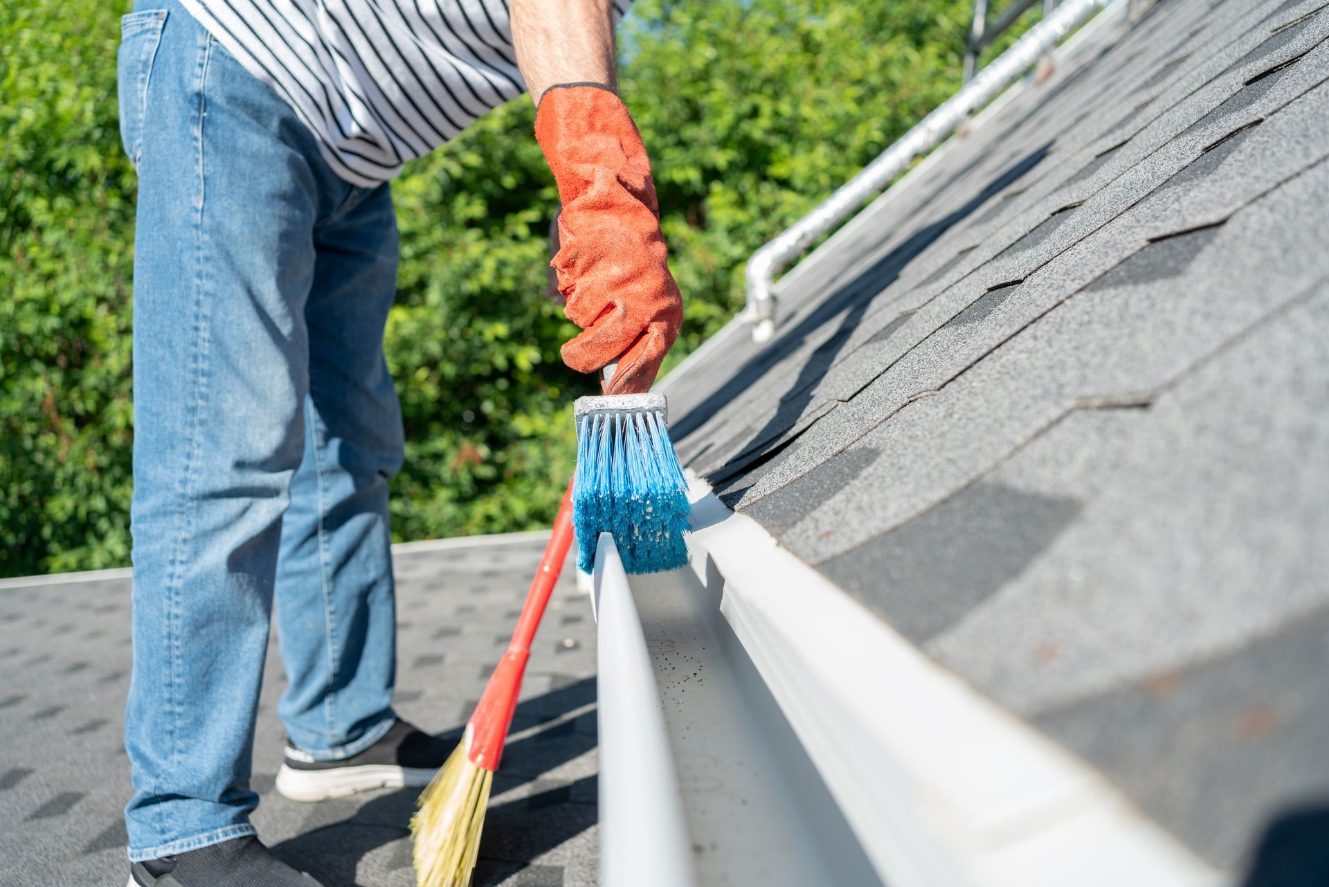 A man is cleaning a gutter on a roof with a broom.