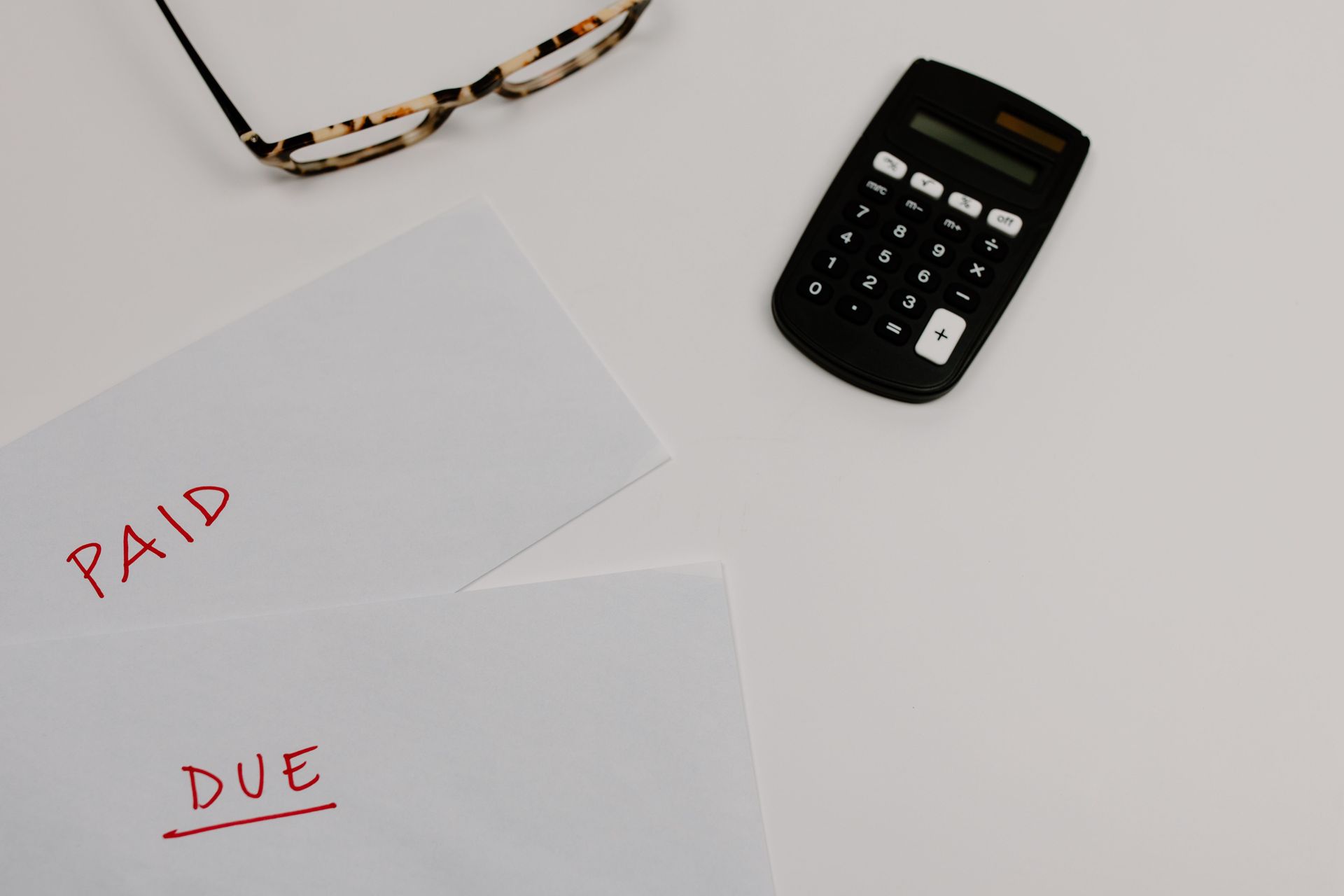 Calculator beside papers labeled “PAID” and “DUE” on a white desk.