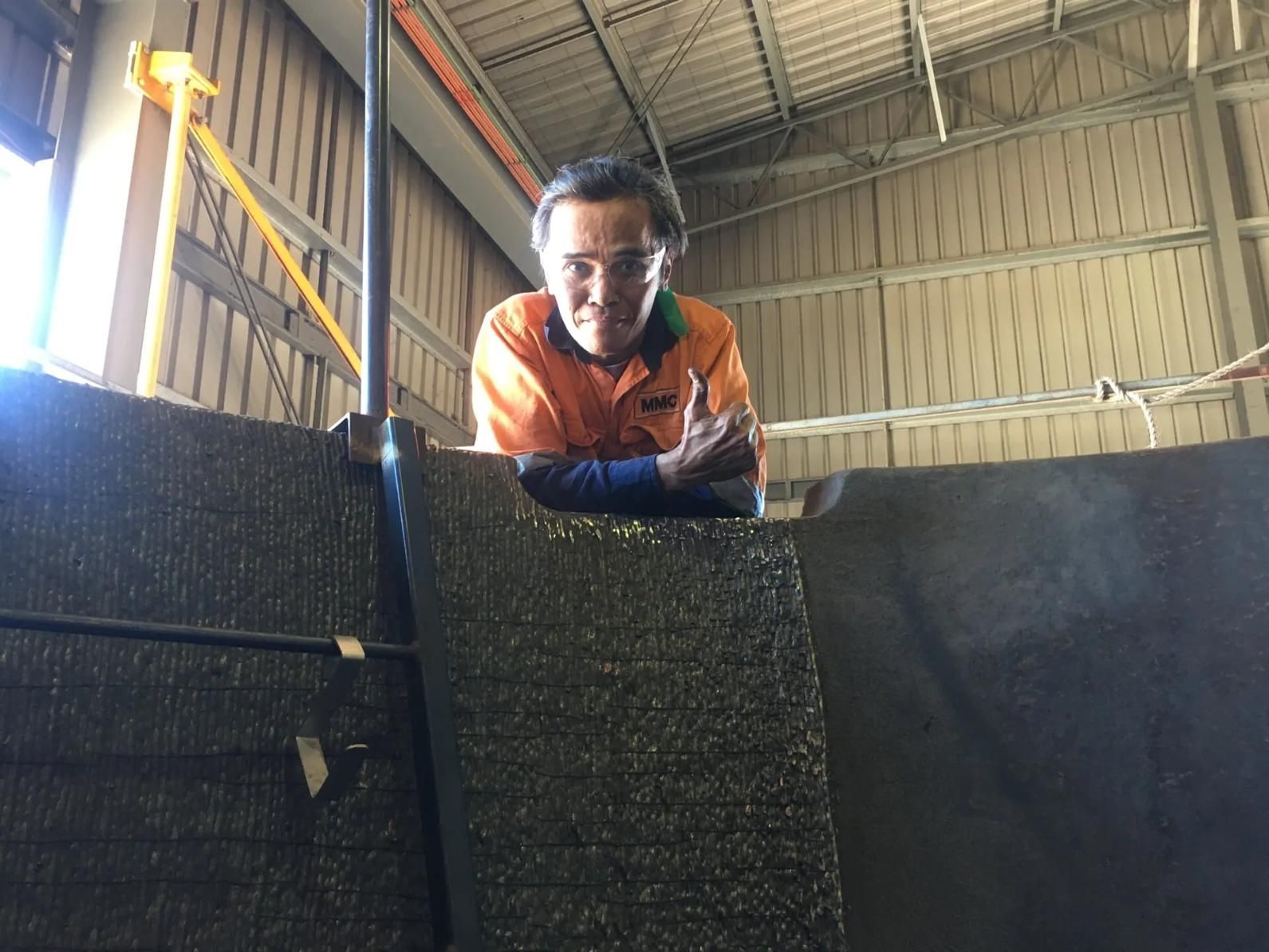 A Man In An Orange Shirt Is Leaning On A Wall And Giving A Thumbs Up — HardRok Engineering Pty Ltd In Mount Isa, QLD