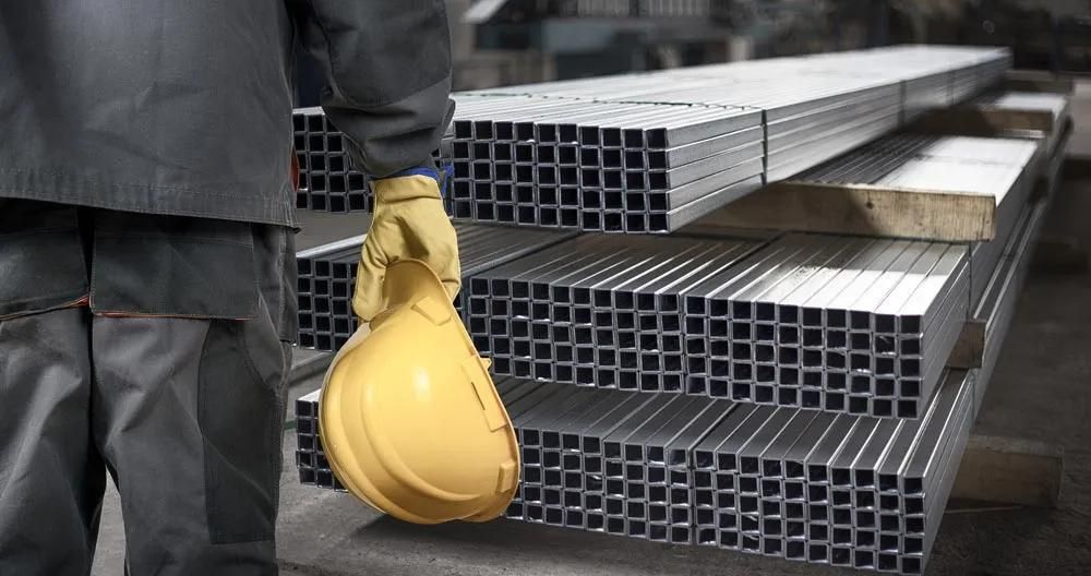 A Worker Holding A Yellow Hard Hat In Front Of A Stack Of Metal Pipes — HardRok Engineering Pty Ltd In Mount Isa, QLD