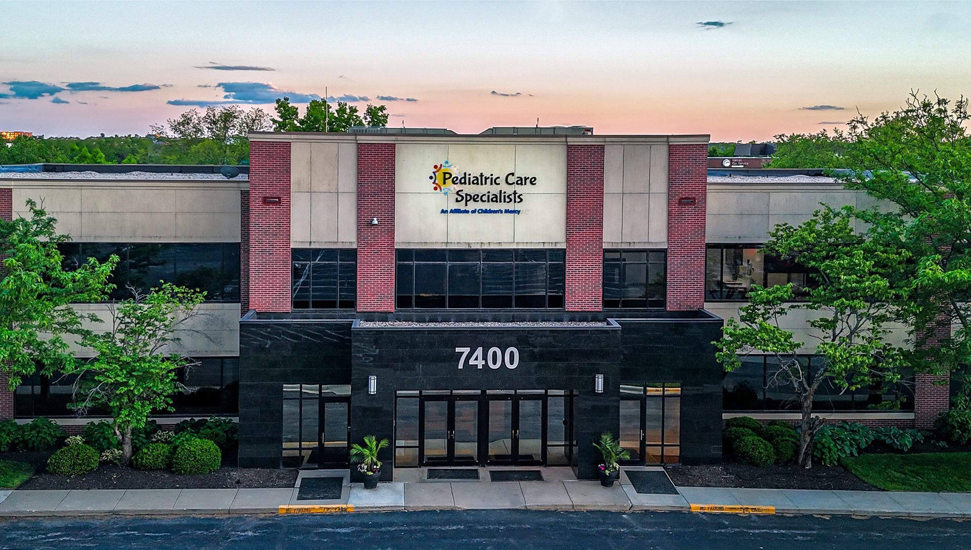 Front view of a modern office building with glass windows, pink columns, and address 7400 at dusk