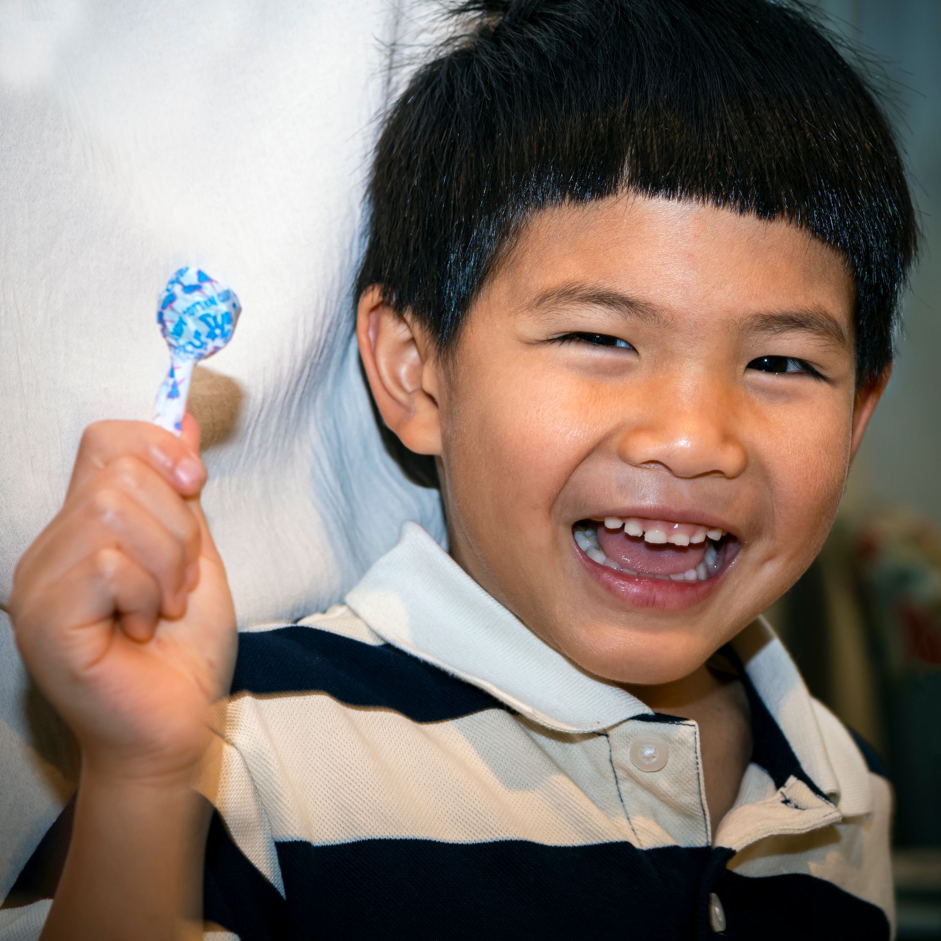 A young boy in a striped shirt is holding a lollipop in his hand.