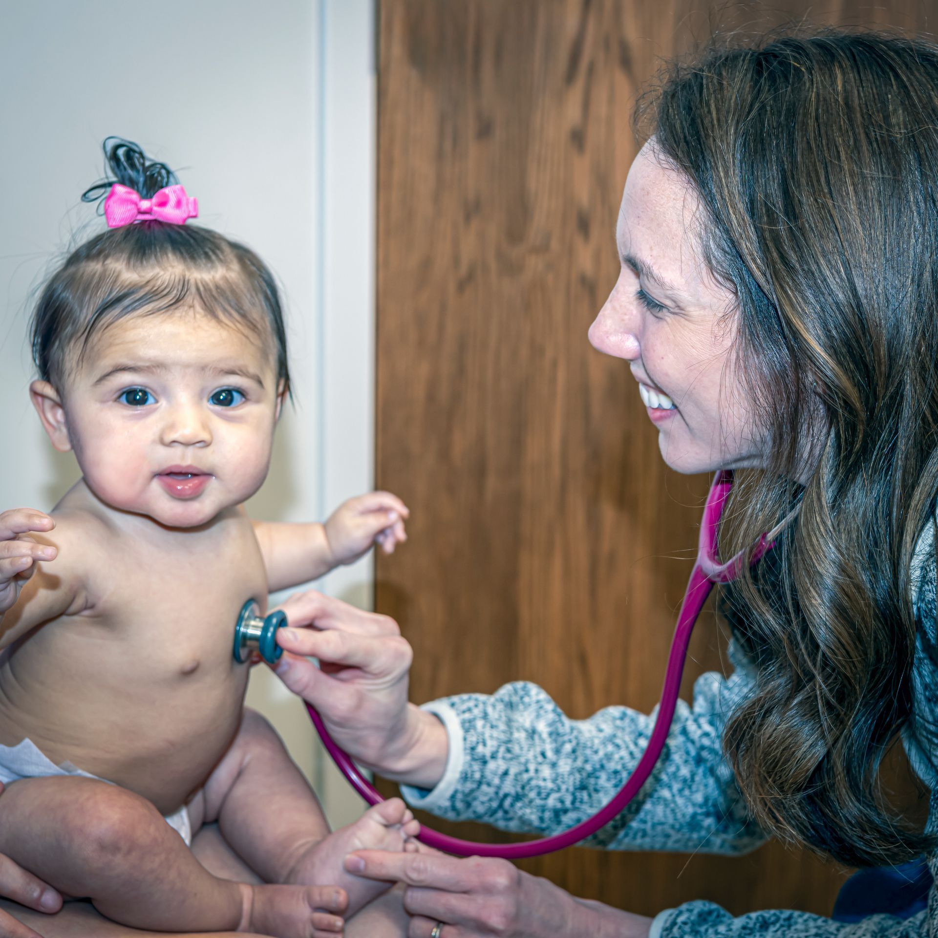 A pediatrician is listening to a baby 's heartbeat with a stethoscope