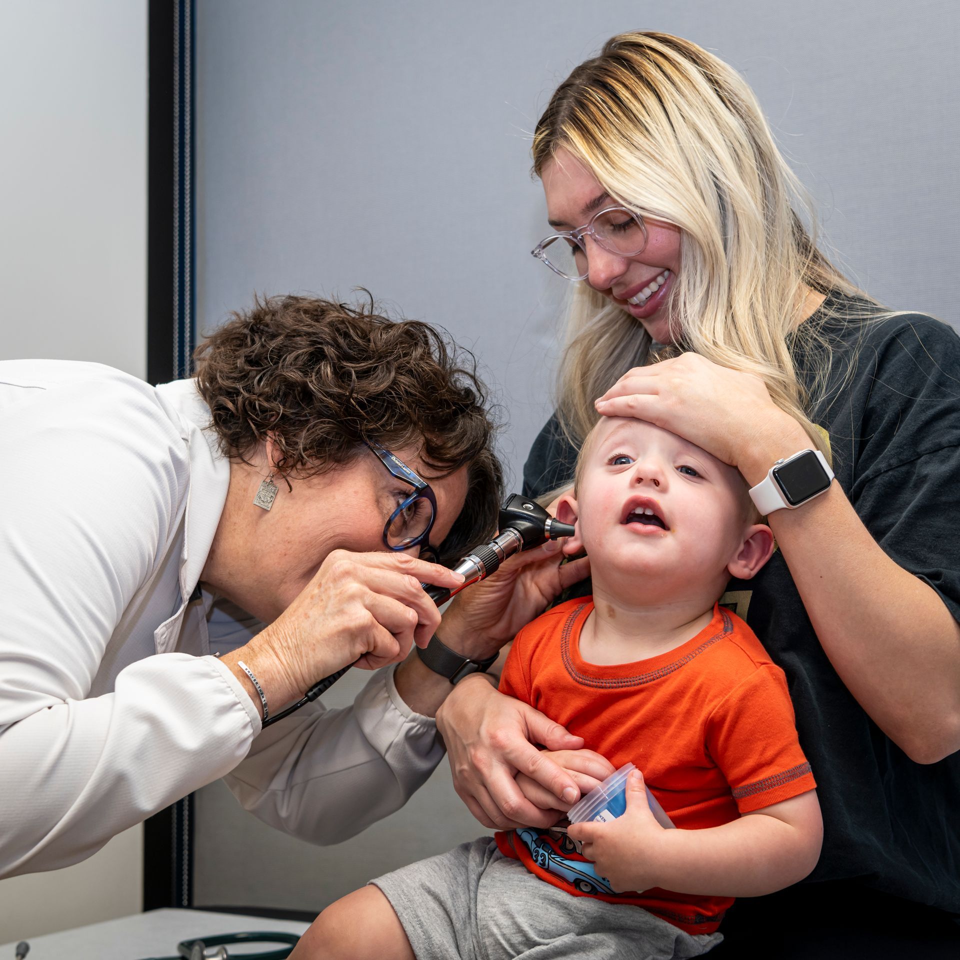 A pediatrician is examining a child 's ear with a stethoscope.