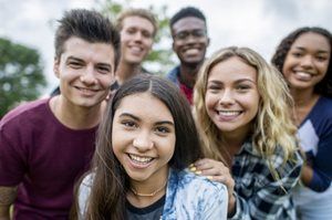 Group of smiling friends outdoors, posing closely together in casual clothes.