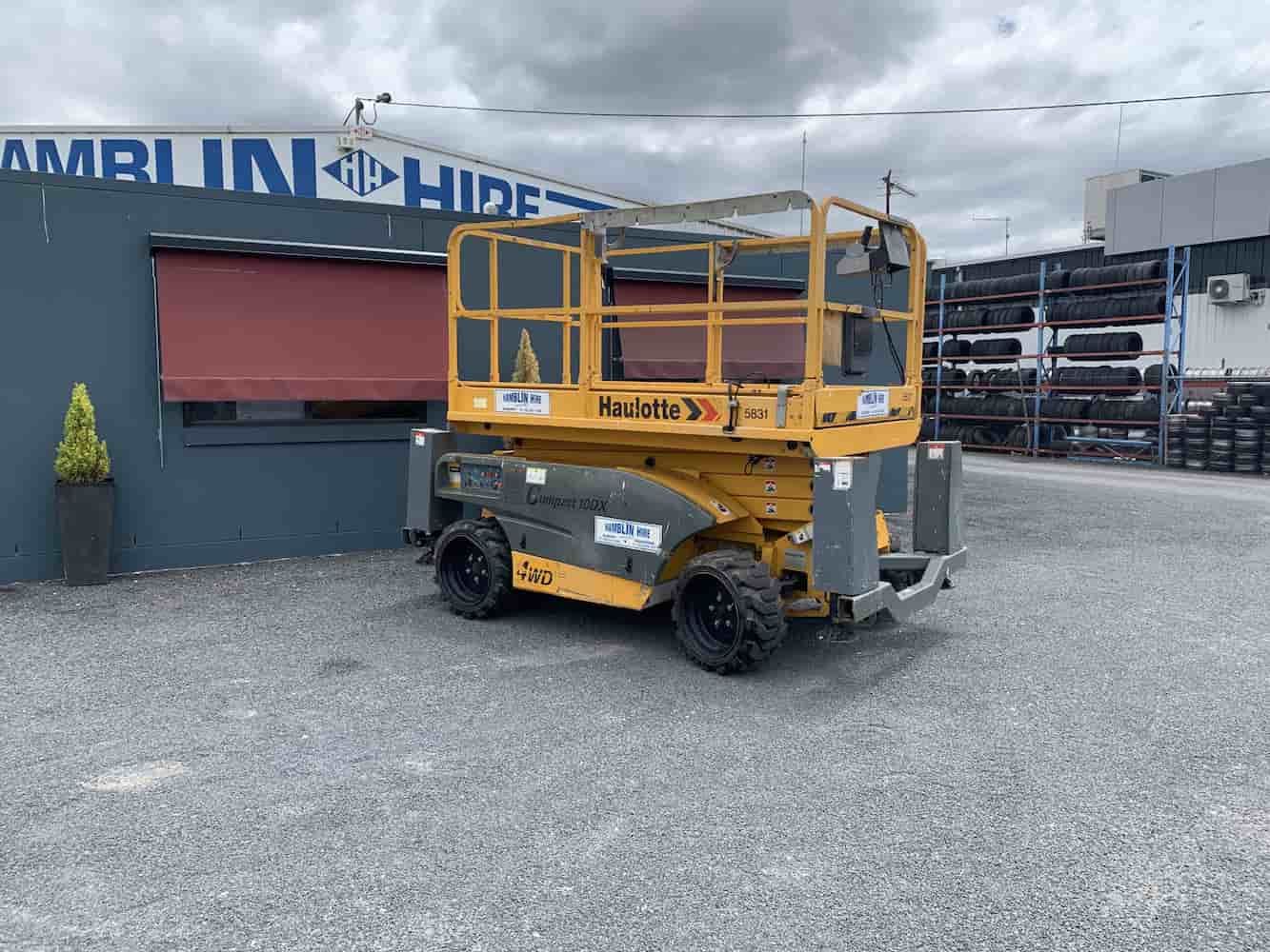 A Yellow Scissor Lift is Parked in Front of a Building — Hamblin Hire in Albury, NSW