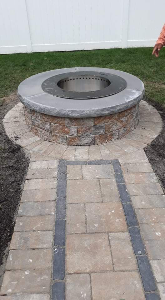 Fire pit with stone base and circular brick path in a backyard.