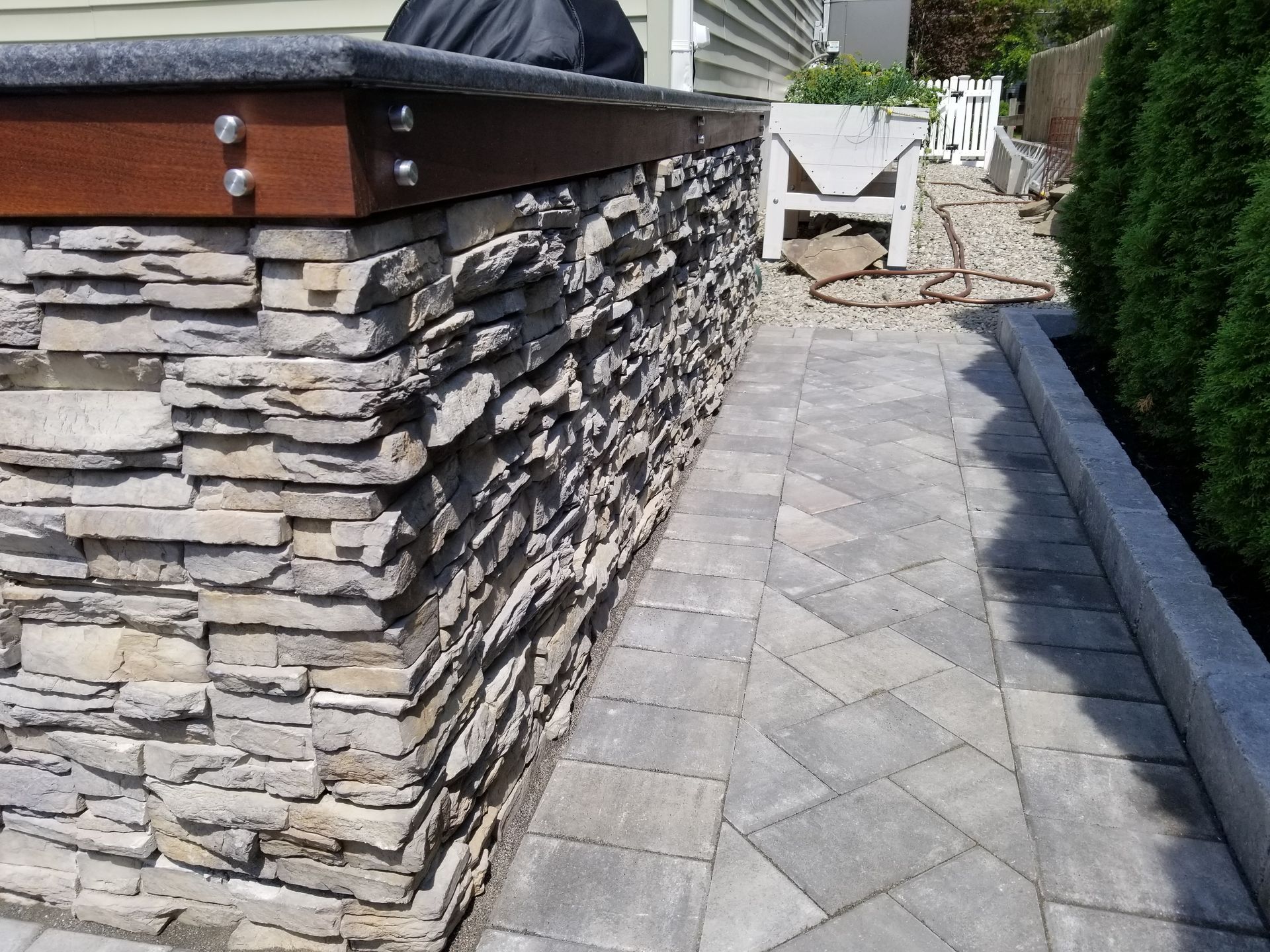Stone wall with a wooden top, next to a paved pathway.