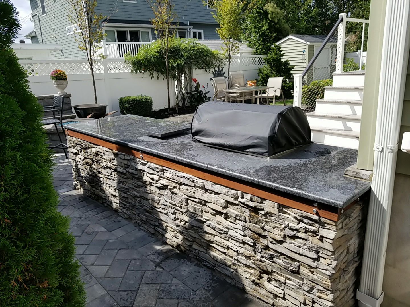 Outdoor kitchen with stone facade, dark granite countertop, and covered grill. Patio setting.