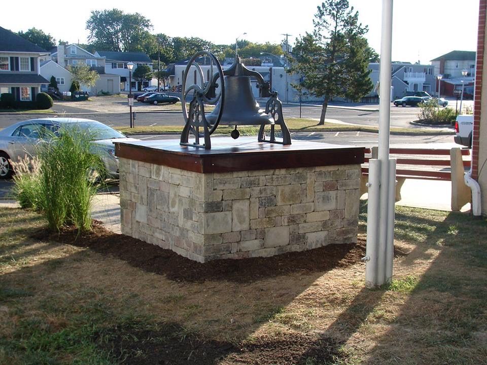Bronze bell on a stone block base, in a town square with buildings and cars.