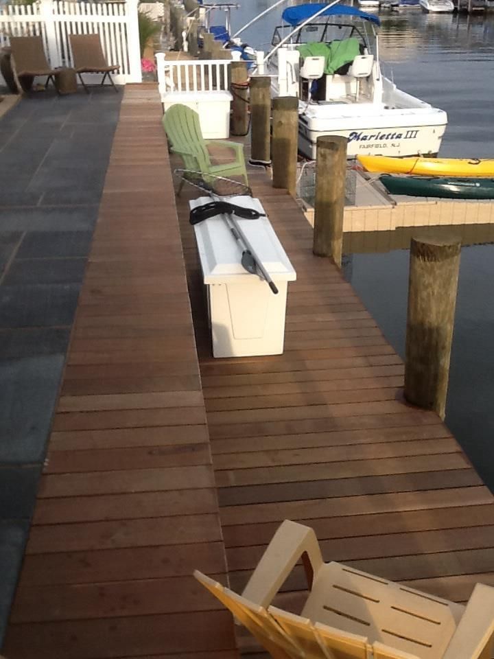 Wooden dock with a boat, chairs, and storage container along a waterway.
