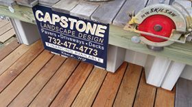 Capstone Landscape Design sign with a skill saw on a wooden deck.
