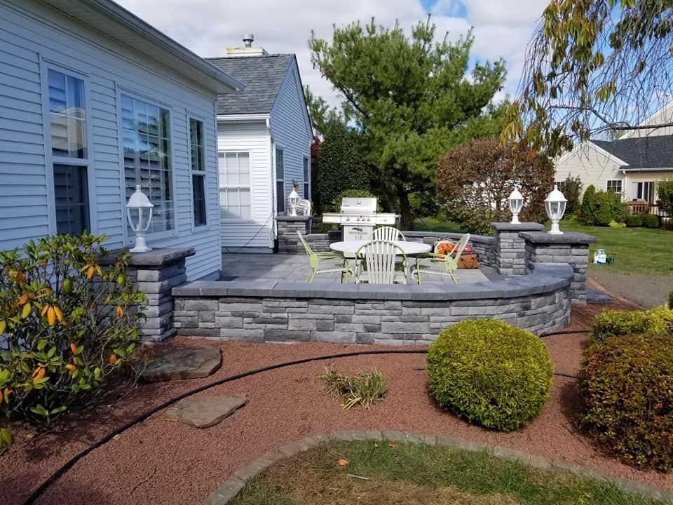 Patio with grilling area, stone walls, white furniture, and landscaping.