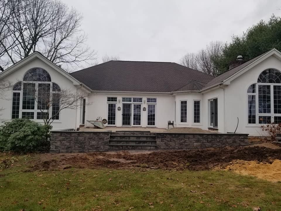 Back of a white house with a stone patio and steps. Brown roof and large arched windows. Overcast day.