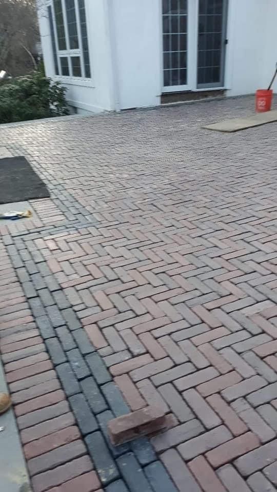 Herringbone brick patio in shades of red and black, with a white building in the background.