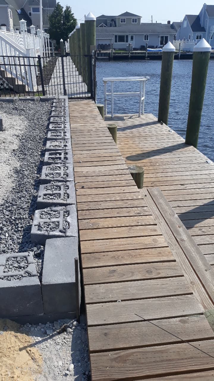 Dock with ramp, retaining wall, water. Gray cement blocks, wooden planks, and black metal fence.