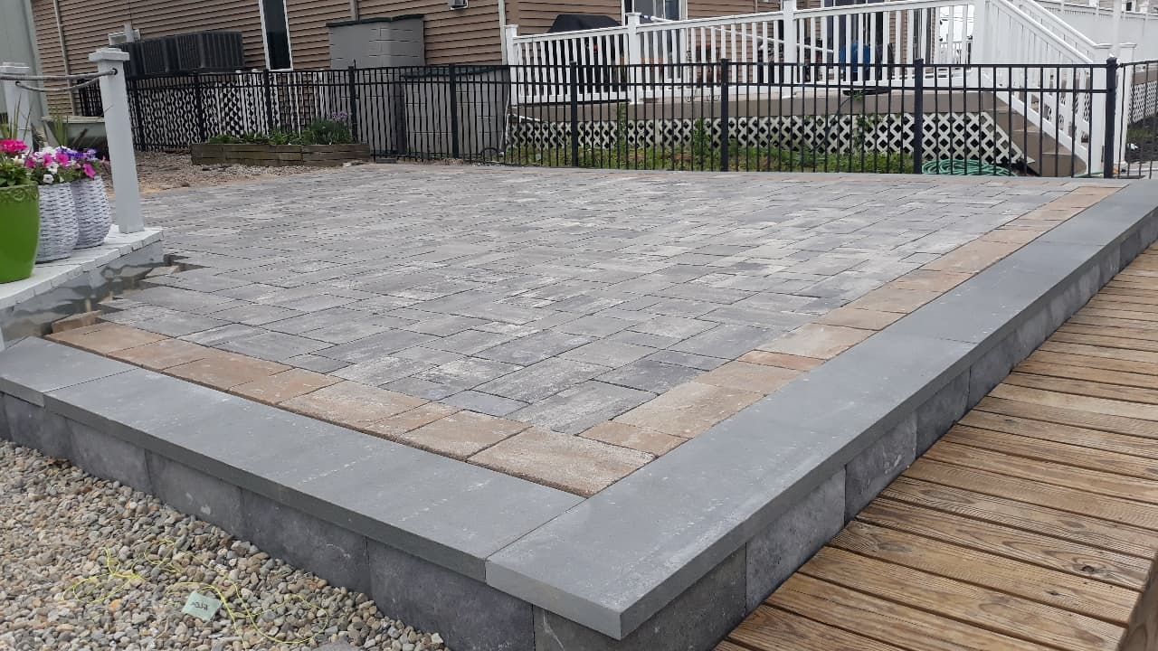 Newly constructed patio with gray pavers and border, next to a wooden deck.
