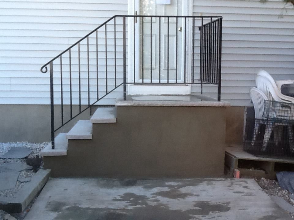 Exterior staircase with black metal railing leading to a white door. Concrete steps and landing.