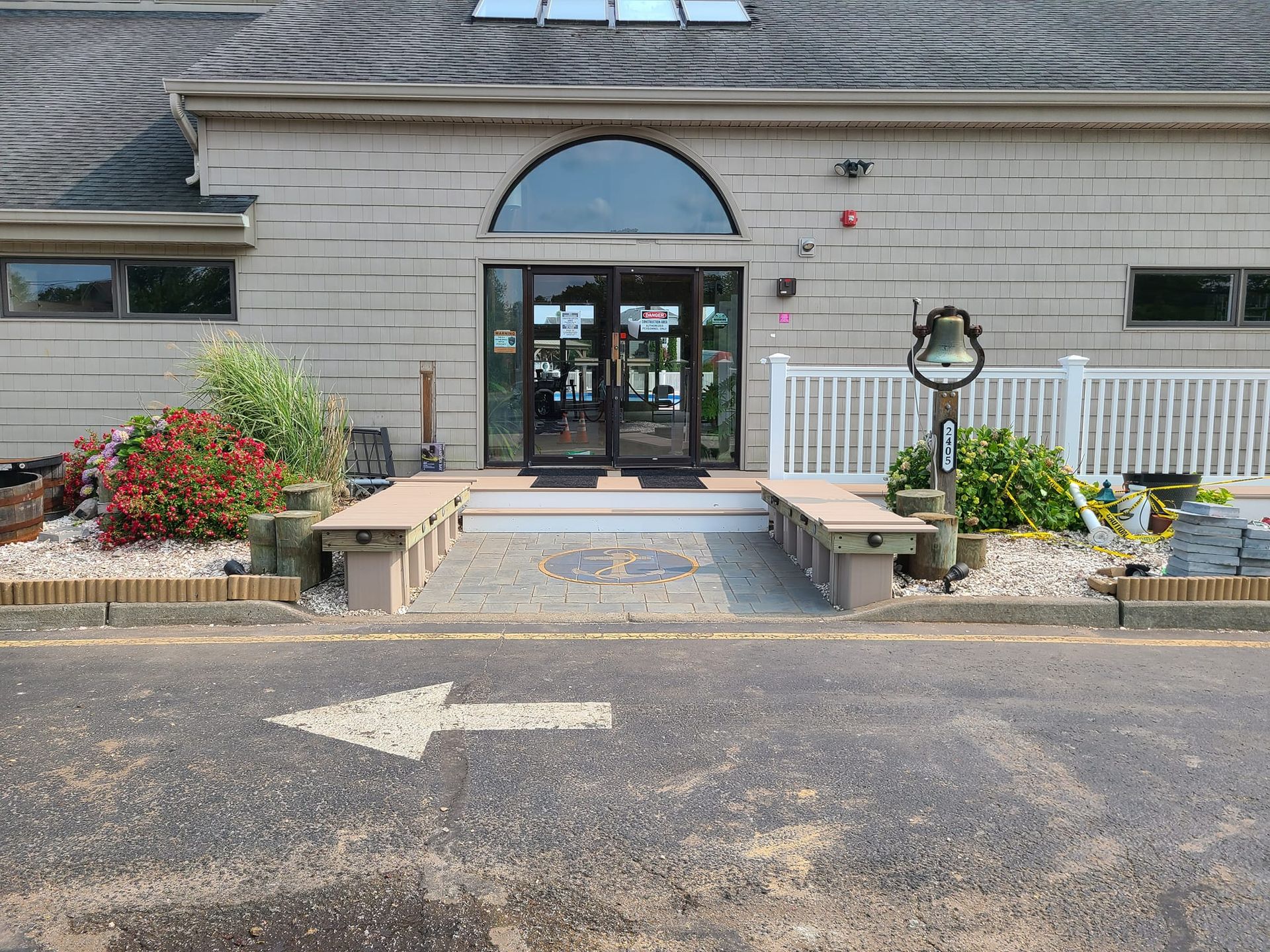 Exterior view of a building with a ramp, benches, and a large door. Arrow on pavement indicates direction.