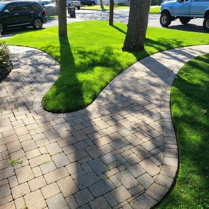 Brick walkway curves through green grass around trees; a truck is in the background.