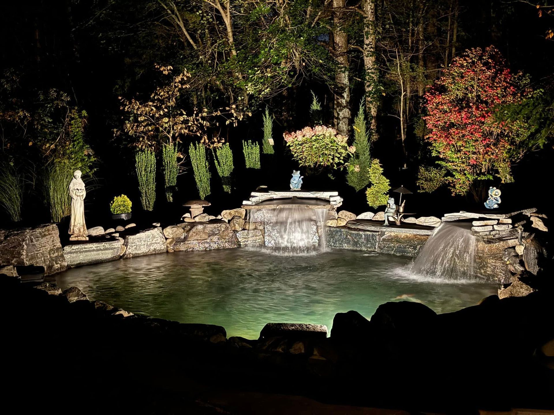 Illuminated water fountain at night with stone accents and surrounding greenery.