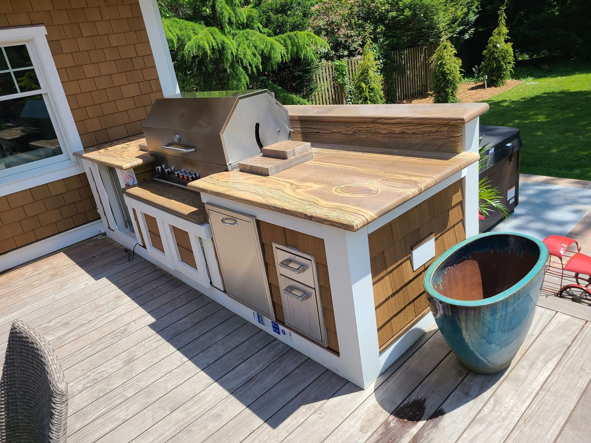 Outdoor kitchen on a wooden deck with grill, built-in storage, and a large turquoise pot.