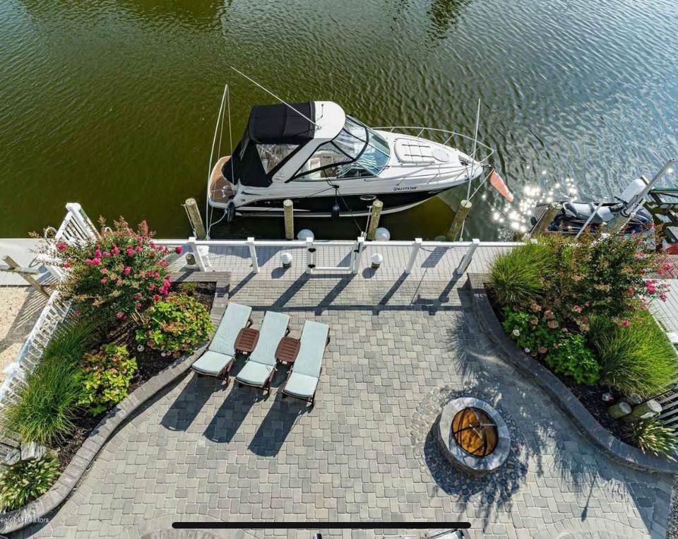 Boat docked by a patio with lounge chairs and fire pit; waterfront view.