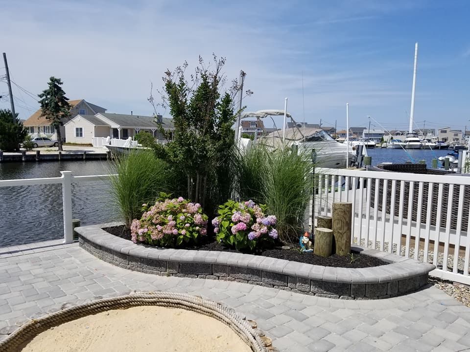 Landscaped flower bed with hydrangeas, ornamental grasses, and fountain, next to a canal.