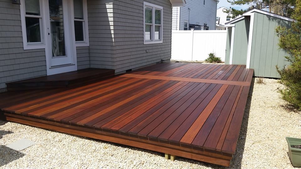 Newly built wooden deck attached to a gray house, set on gravel.